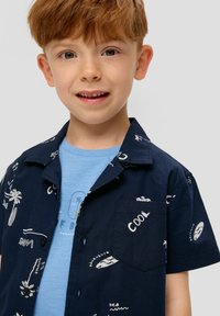 Korte mouwen marineblauw shirt met witte tropische print, voorzien van een zak en een lichtgewicht ontwerp, gedragen over een lichtblauw shirt.