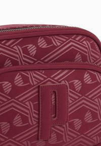Roter Rucksack mit einem geometrischen Präge-Muster, glattem Material und einem deutlich sichtbaren Buchstaben "P" Patch auf der Vorderseite.