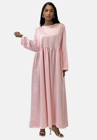 Longue robe rose en satin avec manches longues, taille froncée et silhouette fluide. Texture lisse et tissu léger.