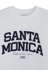 Felpa bianca con testo ricamato blu navy, "SANTA MONICA," e testo più piccolo sottostante che recita "California Ocean Avenue 1985."