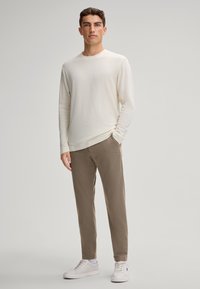 Lichtbeige long-sleeve shirt in combinatie met lichtbruine slim-fit broek en witte sneakers. Soepele stof, eenvoudig ontwerp en relaxed fit.