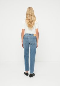 Κλασικά μπλε τζιν με ίσια γραμμή, πέντε τσέπες και δερμάτινο ταμπελάκι στη πίσω ζώνη μέσης. Φορεμένα με λευκό μπλουζάκι και μαύρα παπούτσια.