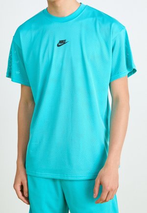 Osoba nosząca turkusową siateczkową koszulkę Nike i pasujące spodenki, widoczna od szyi do połowy uda, z małym czarnym logo Nike na piersi.