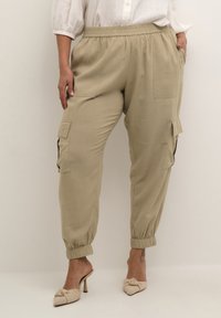 Pantaloni cargo khaki con vita elasticizzata, tasche laterali e polsini affusolati, realizzati in un tessuto leggero e caratterizzati da una superficie liscia.