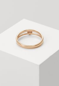 Roze gouden ring met een gladde, gepolijste oppervlakte en een dunne band, die eenvoudig en cirkelvormig lijkt, geplaatst op een wit displayblok.