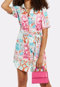 Vestido de manga corta con estampado floral multicolor que incluye tonos rosa, naranja y aqua. Incluye un cinturón y un bolso rosa con asas de cuentas.