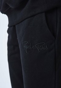 Zwarte sweatpants met een geborduurd logo, een gladde textuur, een elastische tailleband en zijzakken voor extra functionaliteit.