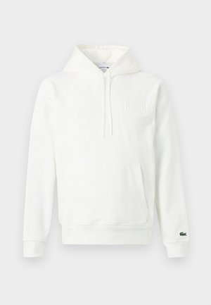 Sweat-shirt blanc à capuche avec poche kangourou avant, fermeture éclair à mi-hauteur et petit logo crocodile vert sur le poignet de la manche gauche.