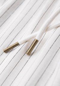 Tissu blanc avec de fines rayures verticales noires comportant deux cordons blancs avec embouts métalliques en laiton.