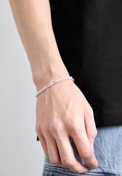 Silver chain bracelet with oval links, featuring a polished finish. Worn on a hand, contrasting against a black shirt and denim.