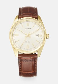 Gold-tone watch with a cream dial, silver hour markers, and date display. Brown leather strap features a crocodile texture. Water-resistant to 50m.