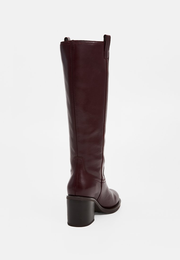 Bota de cuero burdeos hasta la rodilla con tacón ancho, con una textura suave y detalles de costura mínimos, diseñada con una punta redondeada.