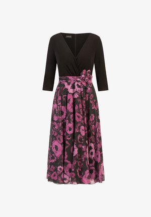 Zwart jurkje met een V-hals en driekwart mouwen, met een rok met een roze bloemenpatroon en een bloemdetail op de taille.