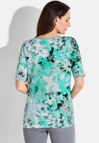 Multikleurige korte mouwen top met een bloemenpatroon in tinten van teal, wit en zwart. Gladde stof met een relaxte pasvorm en ronde halslijn.