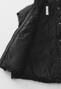 Schwarze gepolsterte Weste mit einem gesteppten Muster, leichtem Stoff, Reißverschluss, offenem Frontdesign und ohne Ärmel. Das Innenfutter ist glatt.