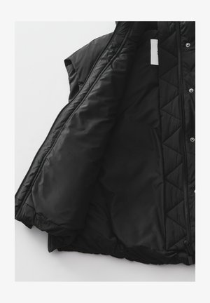 Gilet imbottito nero con motivo trapuntato, tessuto leggero, chiusura con zip, davanti aperto e senza maniche. Fodera interna liscia.
