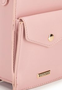 Borsa a mano in pelle rosa con una tasca frontale, dettagli in oro e cuciture decorative. Presenta un'etichetta del marchio visibile nella parte inferiore.