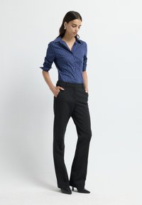 Blauw gestreepte button-up shirt en zwarte op maat gemaakte broeken. Het shirt heeft een kraag en opgerolde mouwen; de broeken hebben een slim fit en puntige hakken.