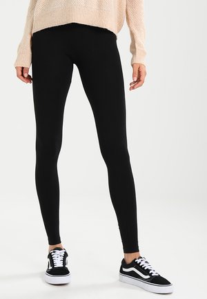 Sorte leggings lavet af strækbart materiale, med en slim fit. Samlet med sorte og hvide sneakers, hvilket skaber et afslappet look.