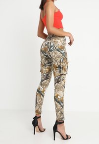 Pantalons cargo camouflés dans des teintes beige, marron et verte. Présente une coupe ajustée, des poches latérales et une taille haute, associés à des escarpins noirs à talons aiguilles.