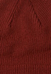Bonnet tricoté rouge avec une texture côtelée et un design conique. Le tissu semble doux et chaud, adapté aux temps froids.