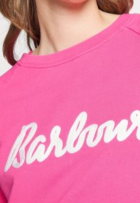 Gros plan d'une personne portant un t-shirt rose vif avec un texte blanc en italique sur la poitrine.