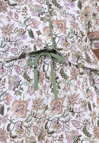 Šaty z měkké bavlny s květinovým vzorem, se zeleným páskem v pase, zdobené růžovými, levandulovými a hnědými botanickými motivy.
