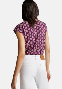 Haut à manches courtes violet avec un motif de feuilles. Associé à un jean en denim blanc avec une patch en cuir sur la taille arrière.