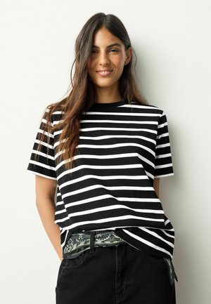 Mustvalge triibuline lühikeste varrukatega t-särk, ümar kaelus. Sobitatud tumedate pükste ja mustrilise vöögiga. Sile kangapind.