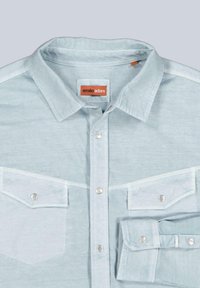 Light blue button-up shirt made of soft fabric. Features a pointed collar, snap buttons, and two chest pockets with decorative stitching.