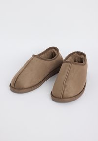 Une paire de chaussons marron à enfiler avec un extérieur en tissu doux et un intérieur en peluche, posée sur une surface blanche.