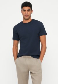 T-shirt in cotone blu navy con collo rotondo e maniche corte, abbinato a pantaloni in lino beige chiaro con vita elastica.