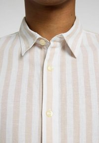 Camisa de rayas crema y beige en tejido ligero. Presenta un cuello con punta, tapeta de botones completa y una sutil textura.