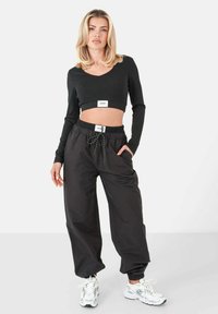 Top negro recortado de manga larga con una etiqueta en el dobladillo, combinado con pantalones negros sueltos que tienen una cintura elástica y cordón.