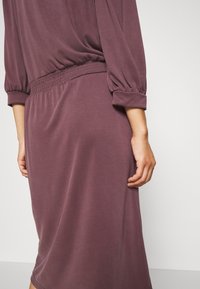 Lila klänning med en avslappnad passform, som har en samlad elastisk midja och trekvartsärmar. Mjuk och slät tygtextur.