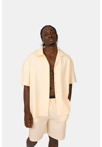 Camicia giallo chiaro a maniche corte con trama a coste e chiusura a bottoni, abbinata a pantaloni corti coordinati. Entrambi presentano una vestibilità comoda.
