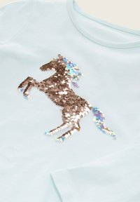 T-shirt azzurro chiaro con un design di unicorno realizzato con paillettes bronzo lucide e iridescenti, completo di dettagli su criniera e coda fluenti.