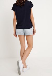 Top de manga corta azul marino con detalles de encaje en los hombros, combinado con pantalones cortos a rayas en azul claro. Zapatillas blancas completan el conjunto.