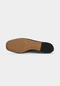 Semelle d'une chaussure en cuir tissé noir avec une semelle en caoutchouc marron, nom de la marque Aldo visible, détails de la taille et zones de grip texturées.