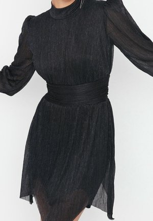 Vestido negro de manga larga con cuello alto, mangas transparentes, cintura ajustada y falda ligeramente acampanada con tejido texturizado y brillante.