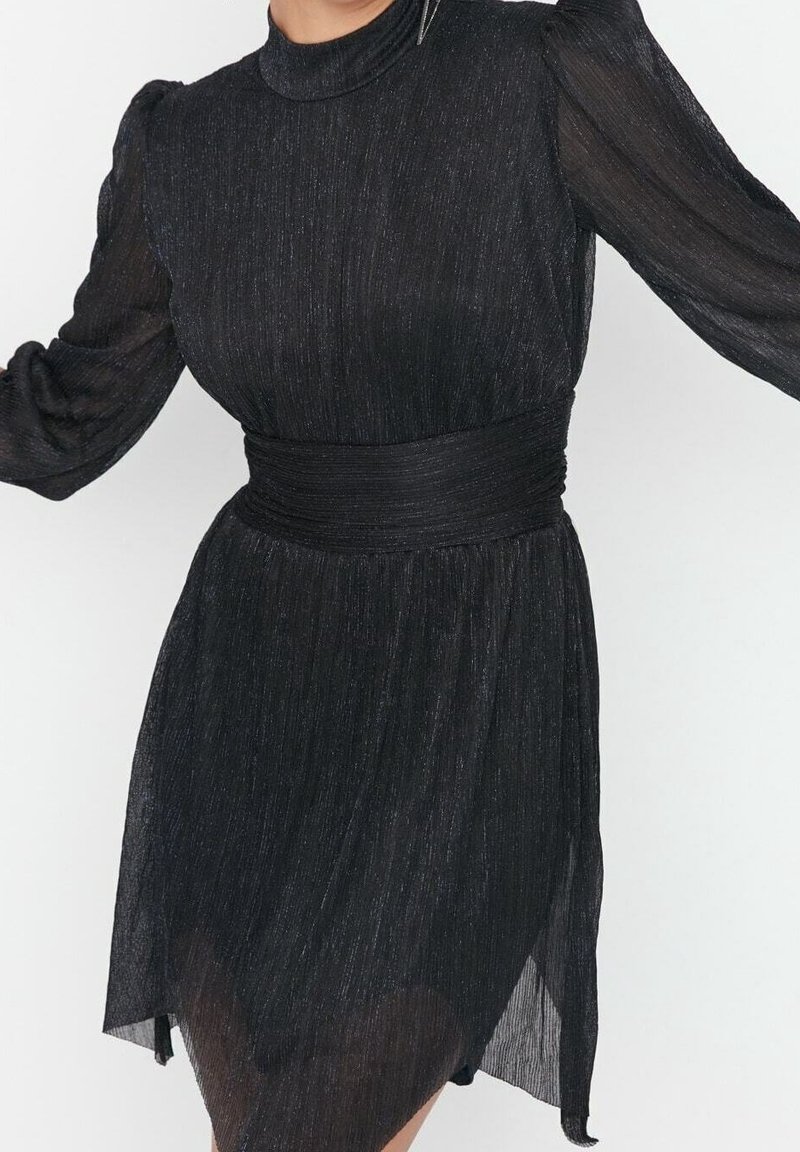 Robe noire à manches longues avec col haut, manches transparentes, taille cintrée et jupe légèrement évasée en tissu texturé et scintillant.