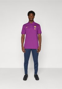 Paarse poloshirt met kraag en logo, gecombineerd met navy broek. Zwarte sneakers maken de outfit compleet. Eenvoudig, atletisch ontwerp.