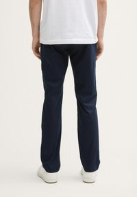 Pantalones de hombre color azul marino, hechos de un tejido con textura suave; presentan un diseño de pierna recta y se combinan con zapatillas blancas.