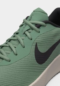 Primer plano de un zapato deportivo verde con tejido texturizado, logo negro de Nike, cordones verde claro y texto "VAPOR LITE" en la lengüeta.