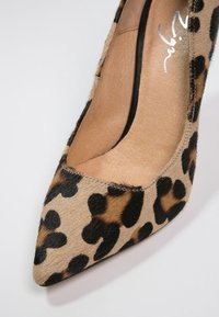 Lodičková bota na vysokém podpatku s leopardím vzorem, která má hladký, texturovaný svršek, špičatou špičku a béžovou koženou stélku.