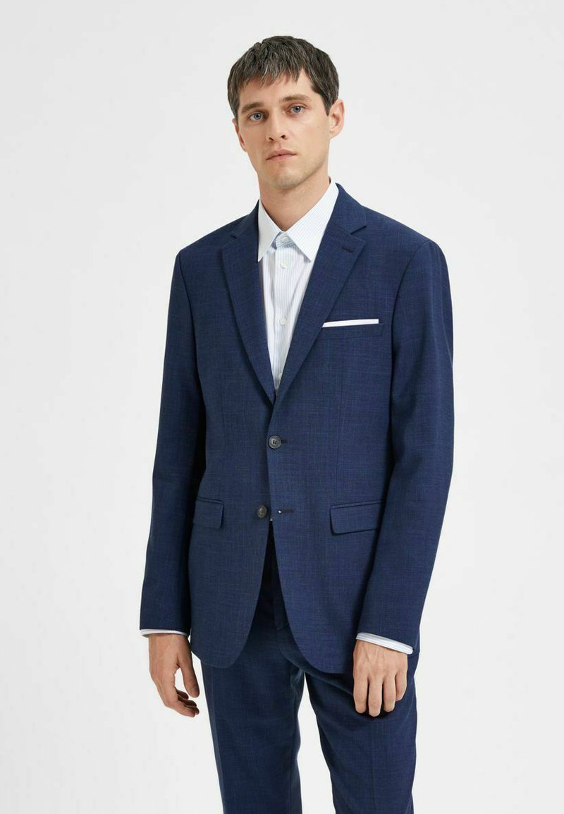 Temno modro blazer iz textured tkanine. Ima dvojno gumbno zapiranje, zarezo na ovratniku in belo žepré. Stilizirano z lahnim črtastim srajcem.