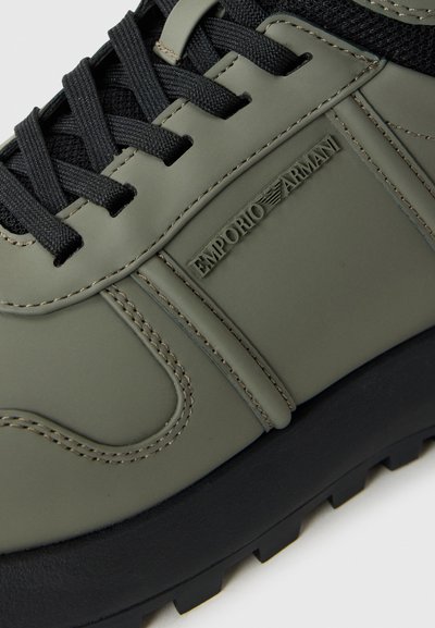 Olive green sneaker with black mesh, textured synthetic upper, thick black rubber outsole, and embossed logo detail on the side.