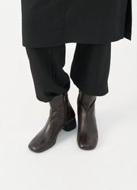 Bocanci de piele maro, cu vârf pătrat, fermoar pe lateral și toc jos, asortați cu pantaloni negri taperi.