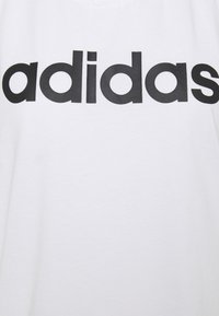 T-shirt in cotone bianco con un grande logo "adidas" nero sul petto. Tessuto liscio e design classico con collo tondo.