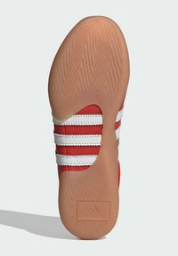 Crvena sportska cipela s potplatom u riblju kost, s tri bijele pruge i utisnutim Adidas logom. Gumeni materijal, fleksibilan dizajn.